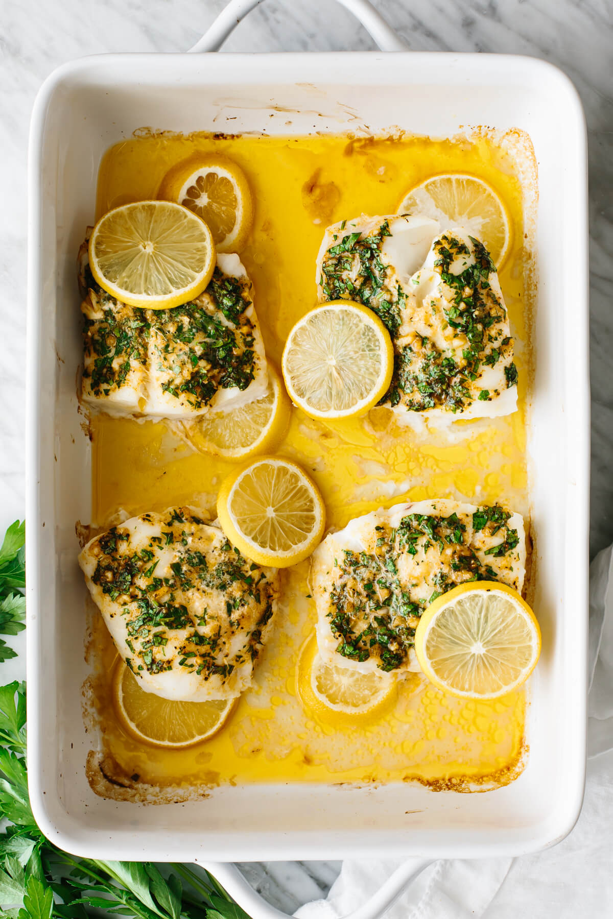 Four baked cod filets in a white casserole dish.