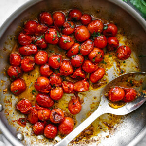 A pan with blistered tomatoes next to a napkin