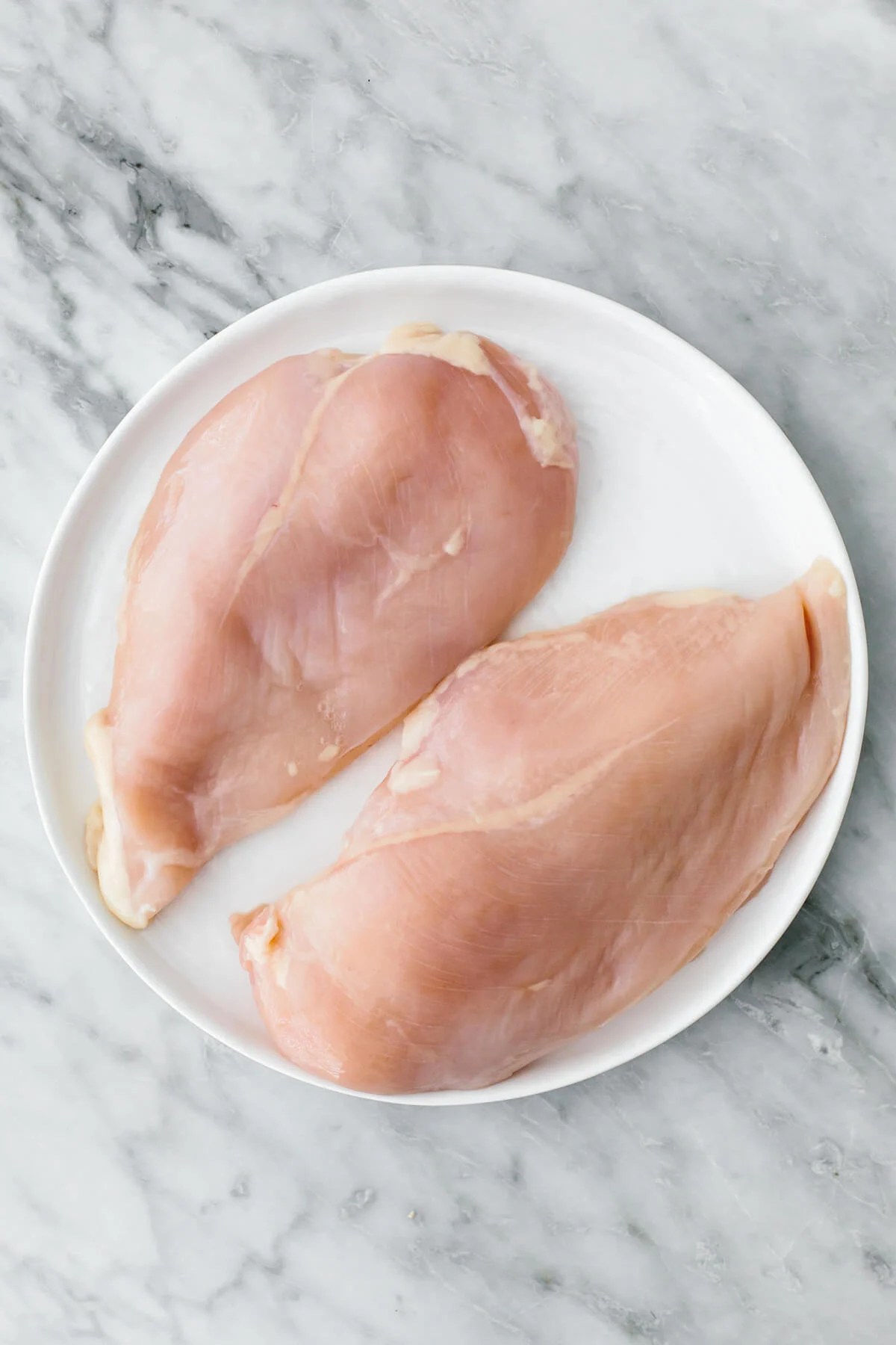 Raw chicken breasts on a plate for chicken marinades.