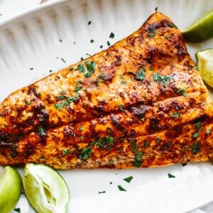 A white plate with chili lime trout and lime wedges