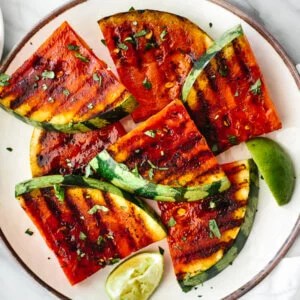 A plate of grilled watermelon slices next to limes.