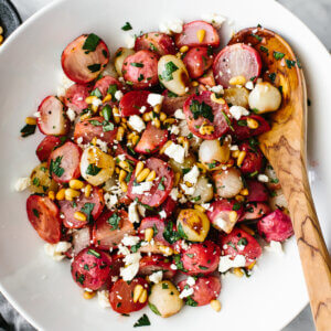Roasted radish salad in a large white bowl next to cheese