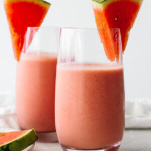 Two glasses of watermelon smoothie with fresh watermelon slices.