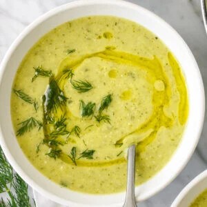 A white bowl of zucchini soup with a spoon
