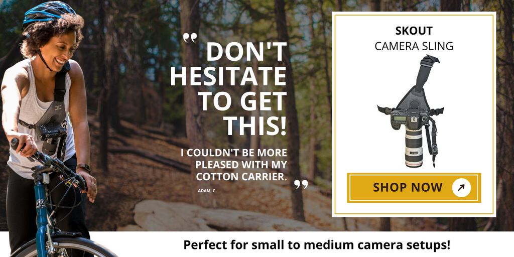 Image of the Skout camera sling, displayed in a retail setting. The photo shows the camera sling being worn by a woman photographer biking, emphasizing its ergonomic design and ease of access. The product image highlights its adjustable strap, durable materials, and convenient camera attachment features, ideal for photographers on the go.